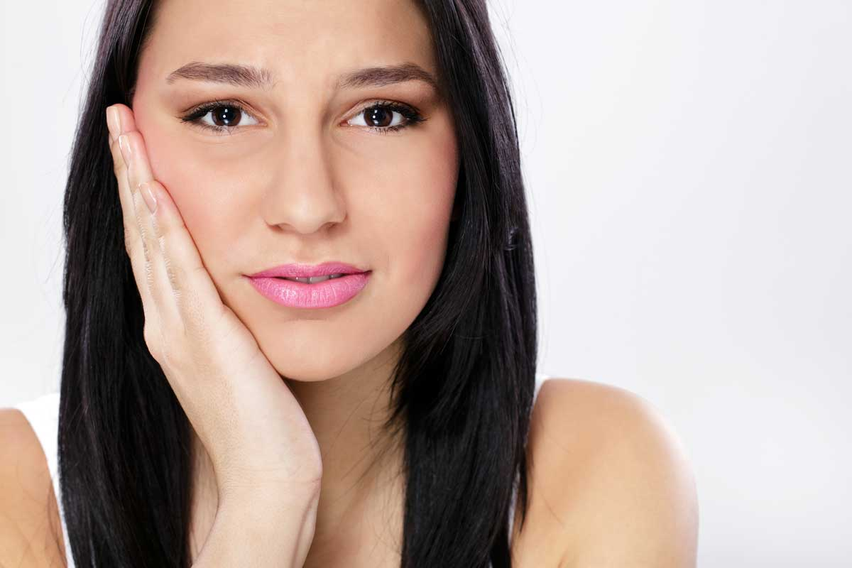 TMJ disorder Hamilton, woman holding her cheek in discomfort from jaw pain caused by a TMJ disorder.