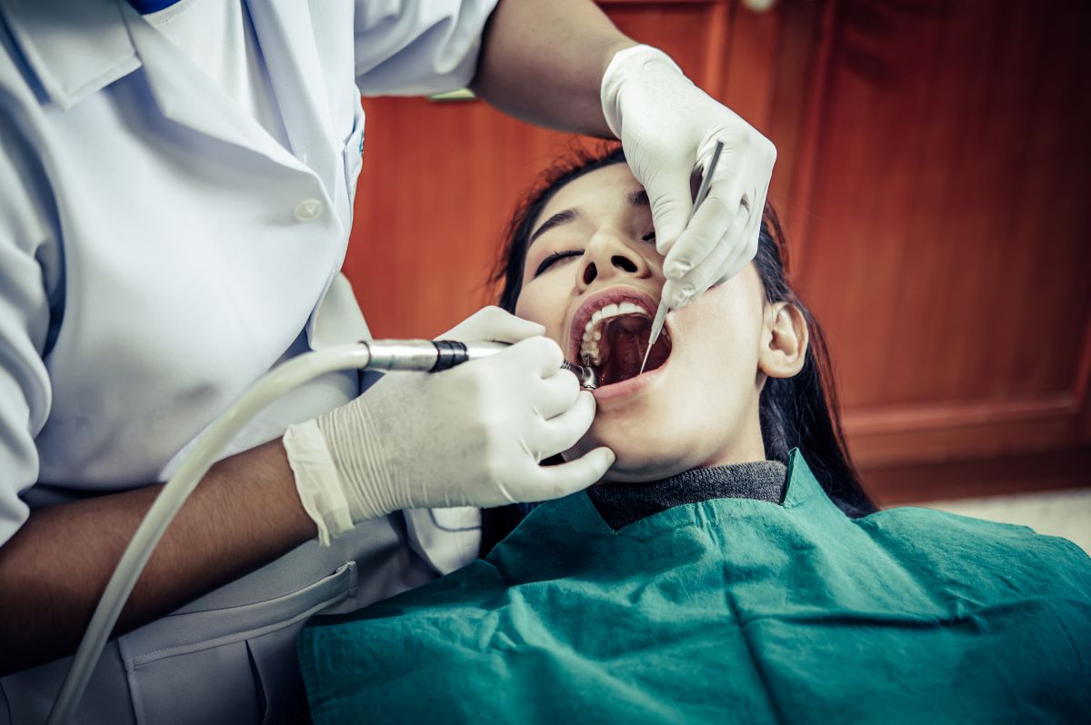 Tooth fillings procedure in Hamilton, Charlton Dentistry dentist using a dental handpiece to gently remove decay before placing a tooth-colored composite filling on a calm female patient